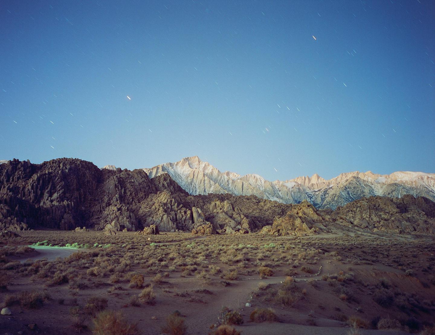 A desert landscape with mountains in the background is illuminated by starlight.
