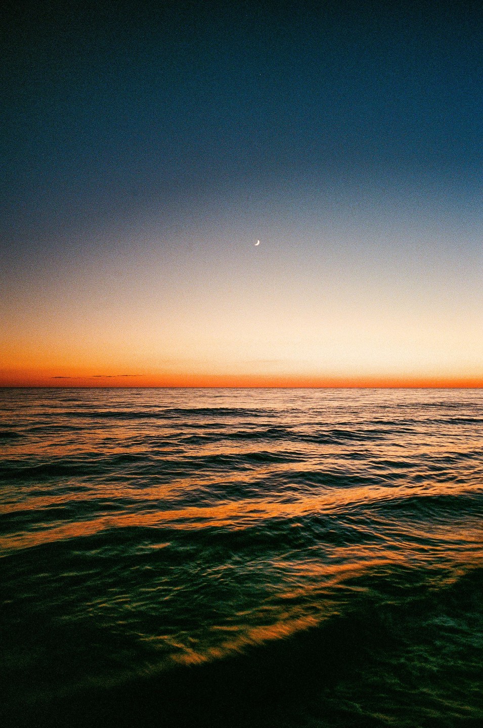 A crescent moon hangs in the sky over the Gulf of Mexico at sunset.