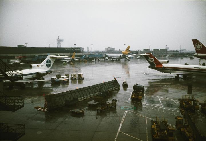 Airplanes are parked on a wet tarmac at Frankfurt Main airport.
