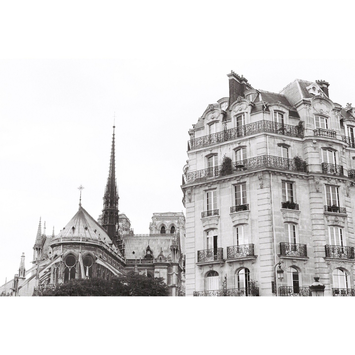 A tall spire of a cathedral rises next to a multi-story building with balconies.