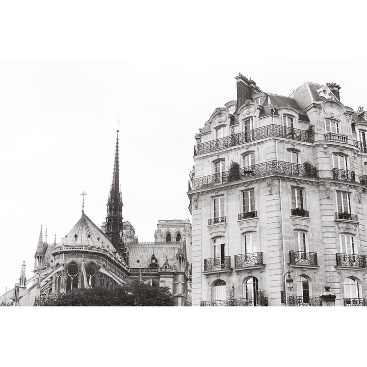 A tall spire of a cathedral rises next to a multi-story building with balconies.
