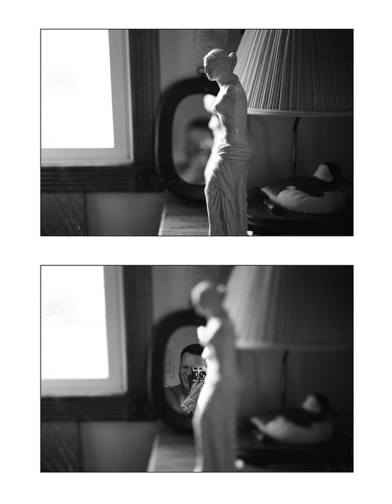 A man takes a self-portrait in a mirror next to a statue and a lamp.