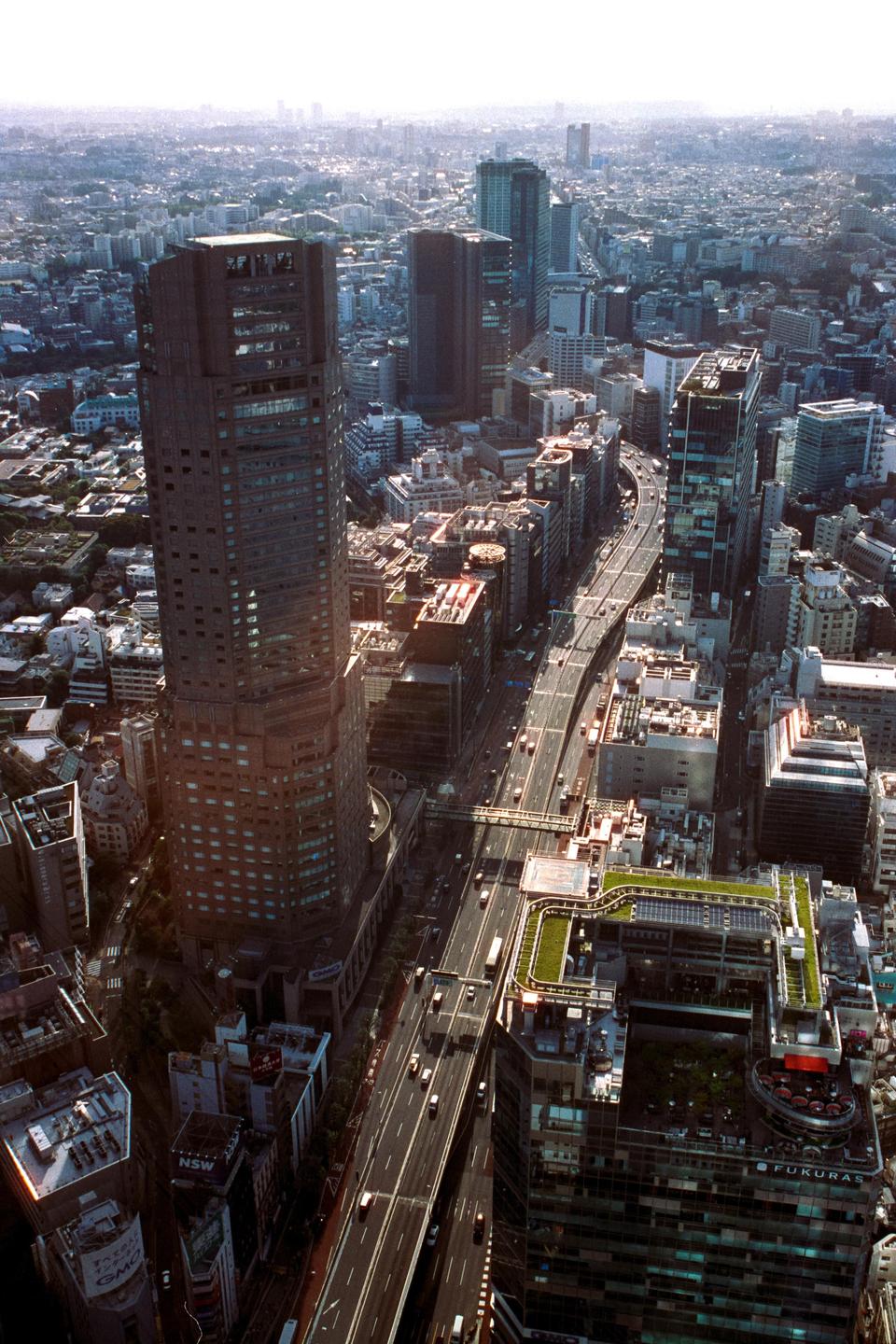 An aerial view shows a highway winding through a dense urban landscape with numerous buildings and a hazy sky.