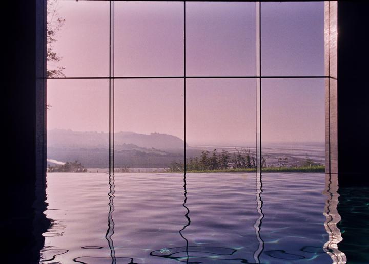 A body of water reflects a window looking out onto a hazy landscape with hills and a body of water.
