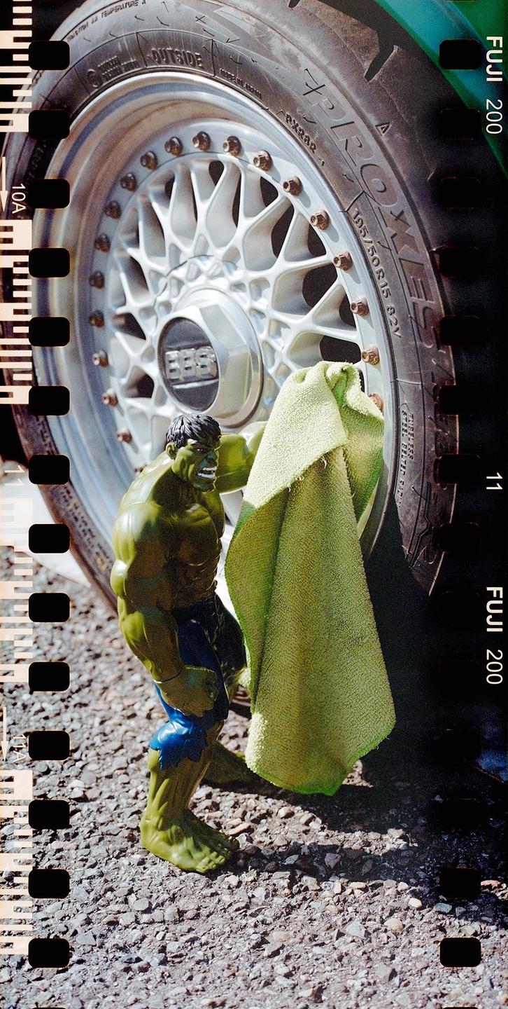 A Hulk action figure is wiping a car wheel with a green cloth.