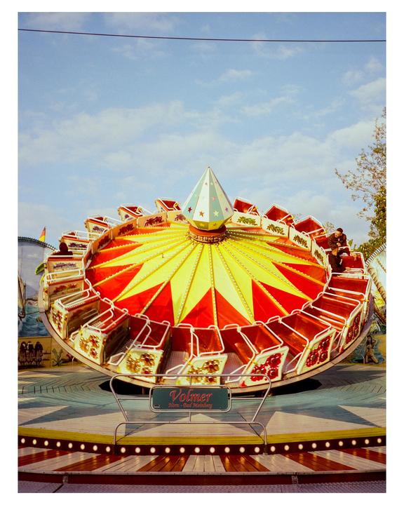 A colorful amusement park ride with red and yellow patterns is captured under a bright blue sky.