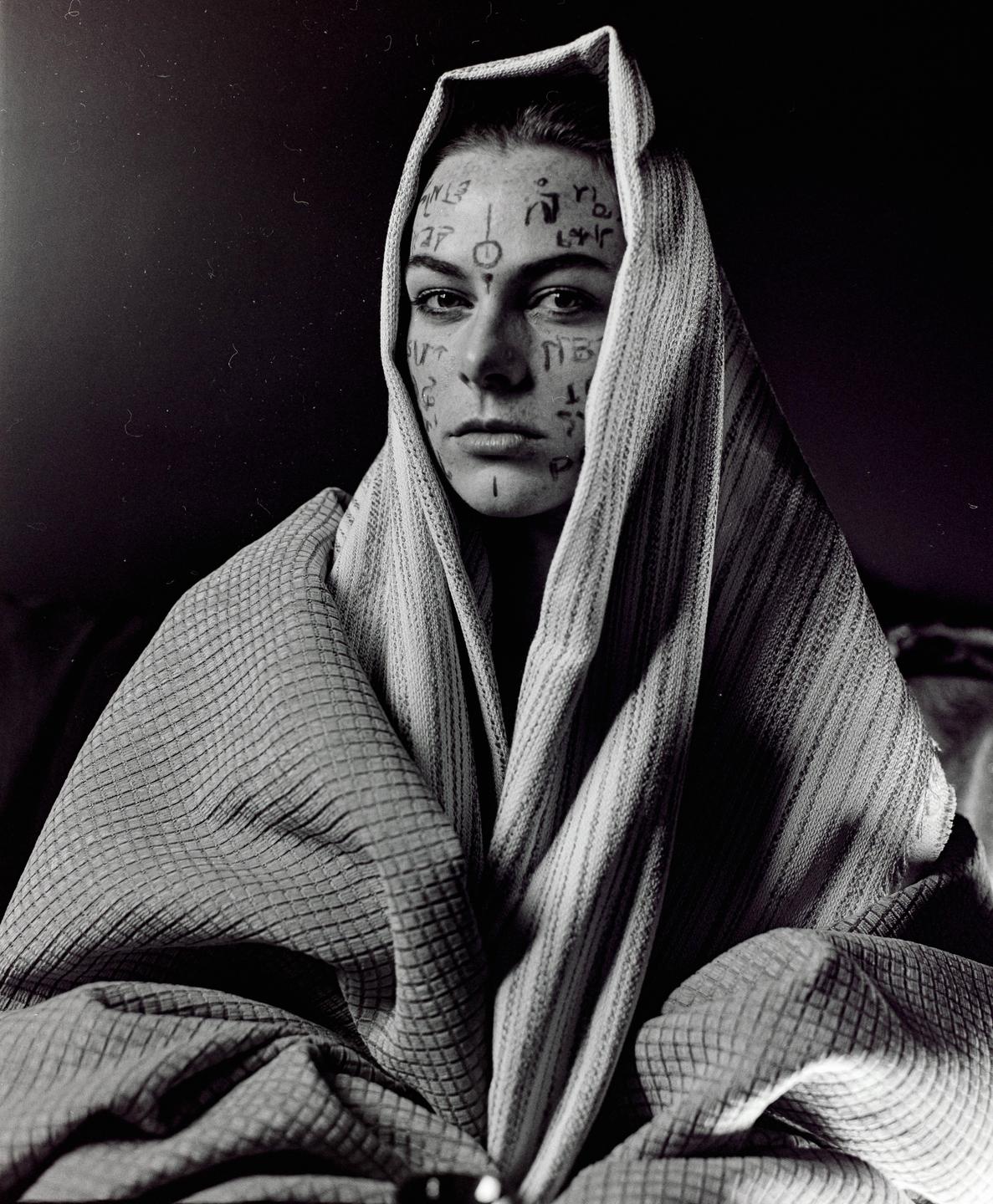 A woman with symbols drawn on her face is wrapped in a patterned fabric.
