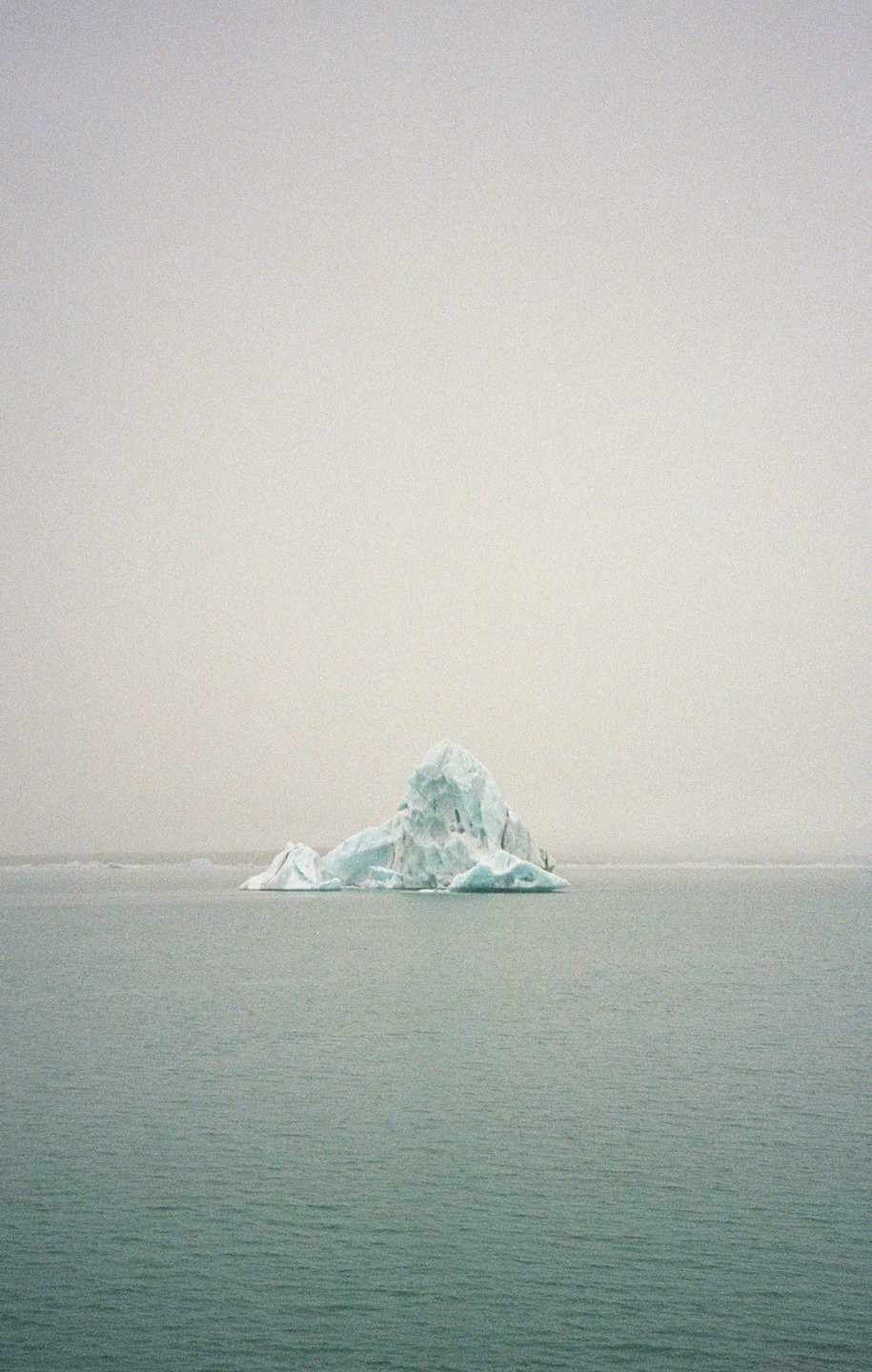 An iceberg floats in the water under a hazy sky.
