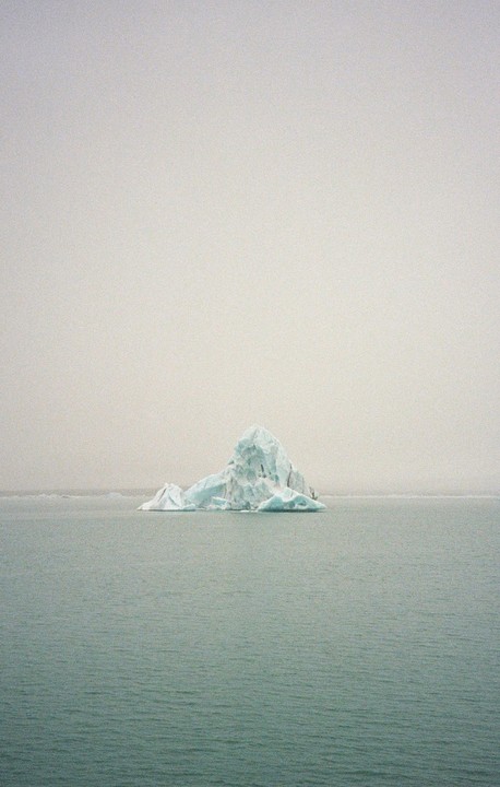 An iceberg floats in the water under a hazy sky.