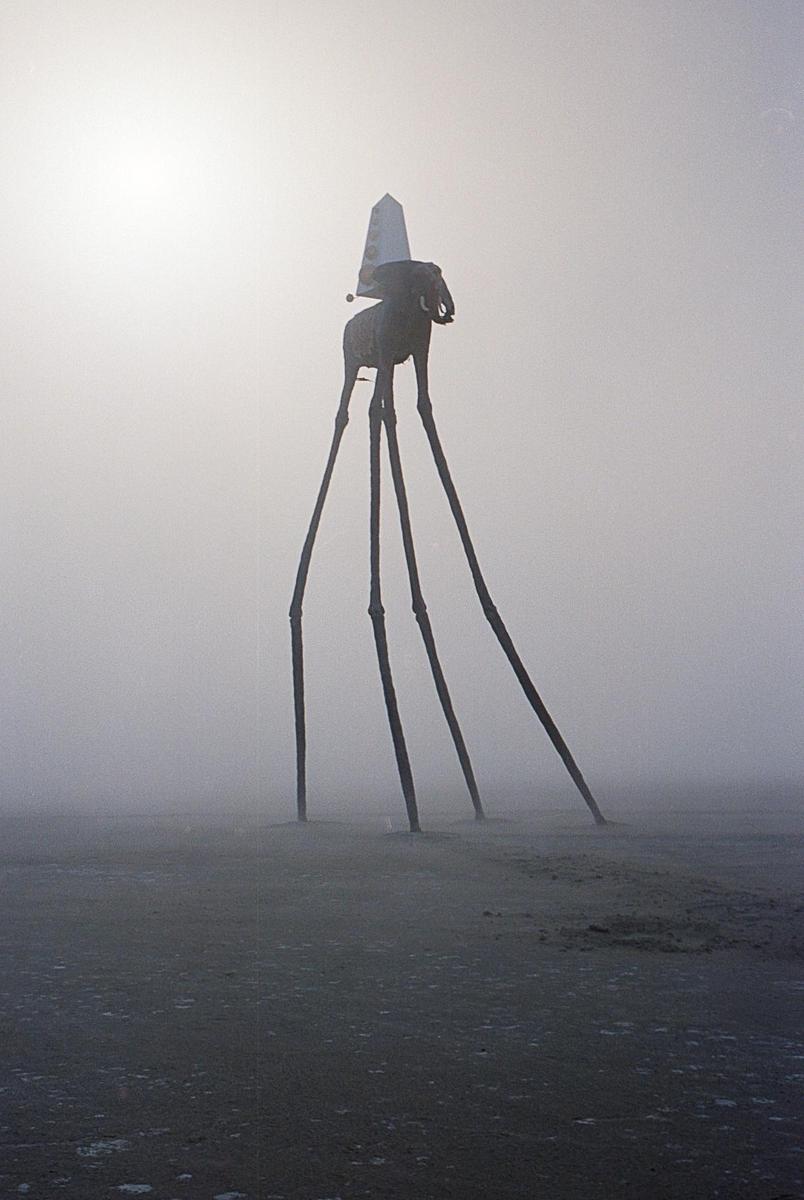 A tall elephant sculpture with a pointed hat stands in a hazy, flat landscape.