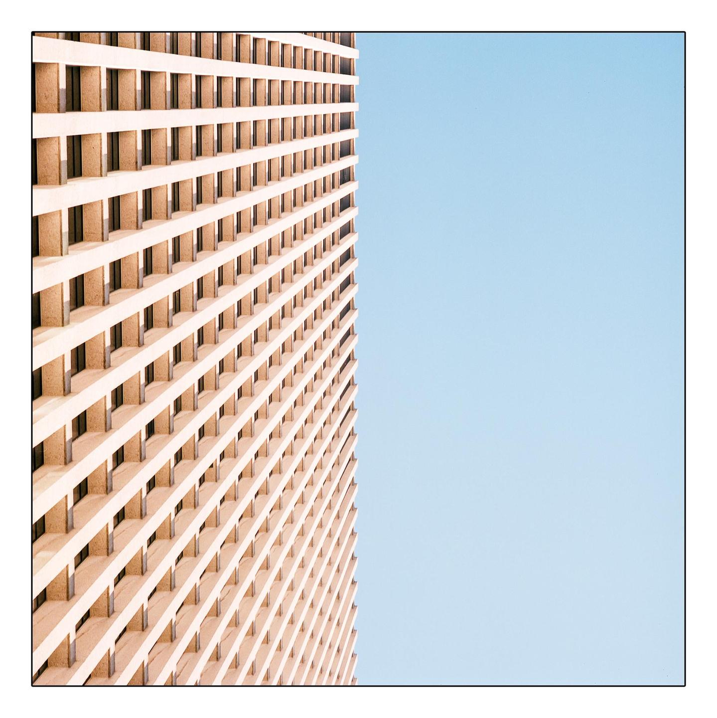 A tall building with a grid-like facade stands against a clear blue sky.