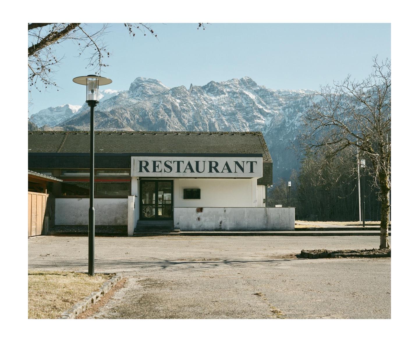 A restaurant building with a large sign is visible in front of a snow-capped mountain range.