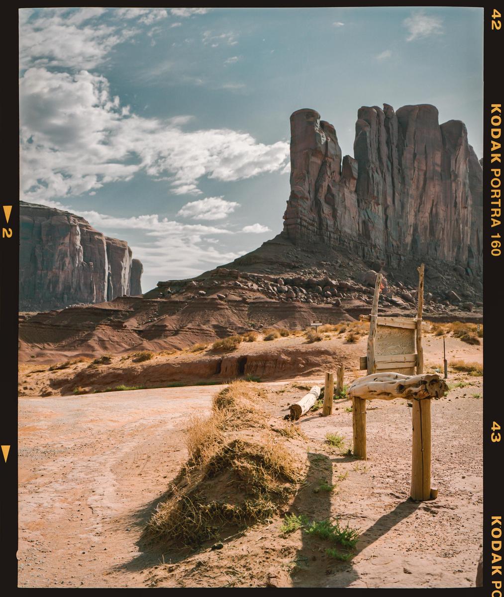 A dirt road leads to a large rock formation under a cloudy sky.