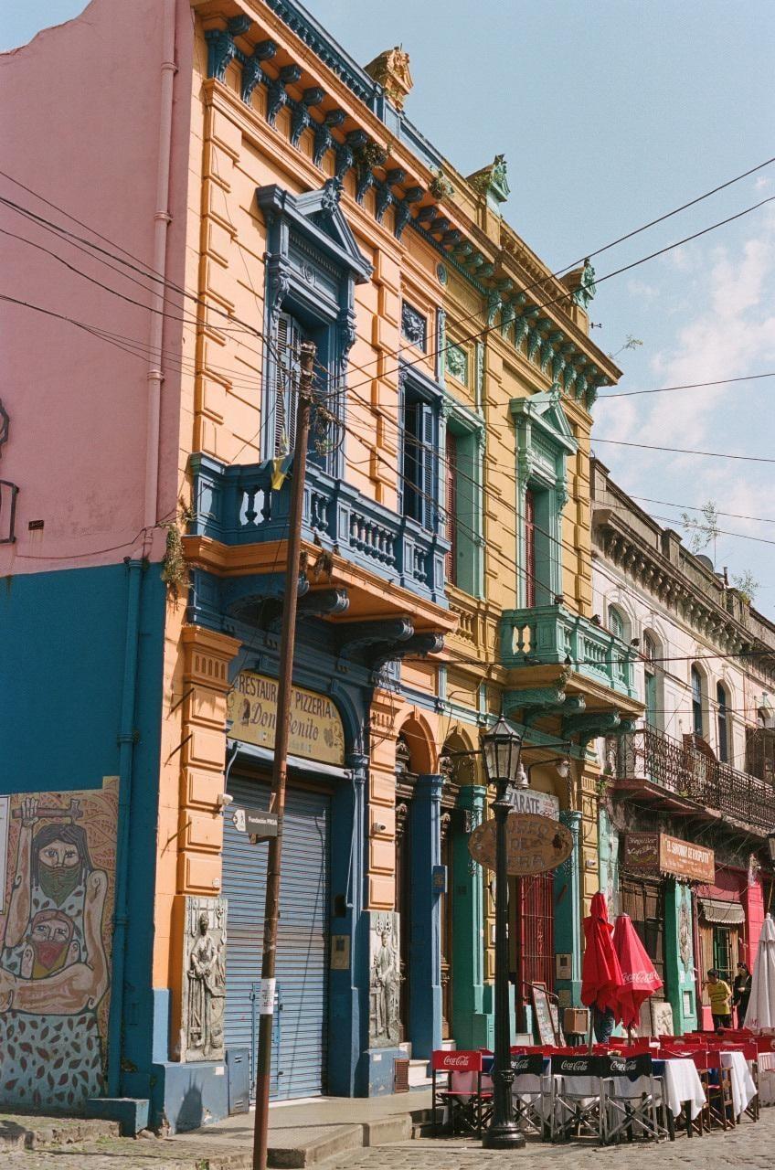 A street in Buenos Aires is lined with colorful buildings and a restaurant with red umbrellas.