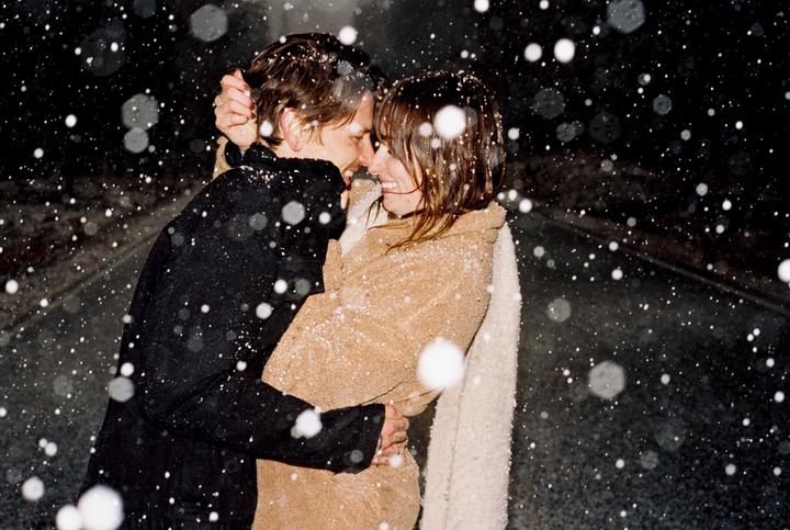 A couple embraces while snow falls around them at night.