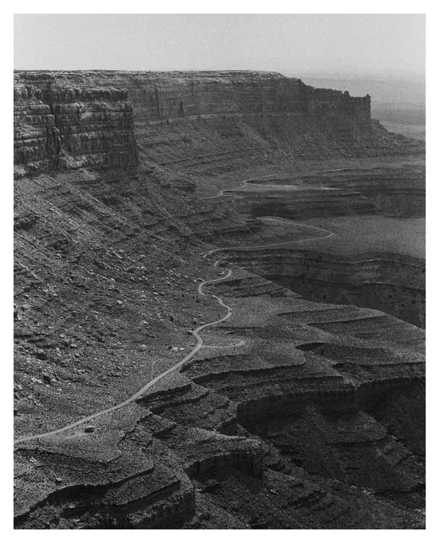 A winding road descends into a vast canyon with towering rock formations.