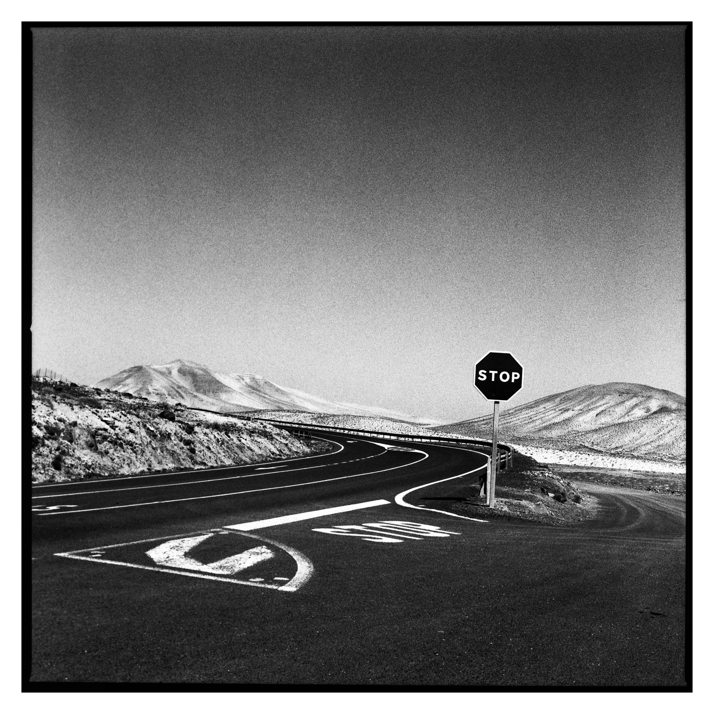 A stop sign stands at a curve in a road with snow-covered mountains in the background.