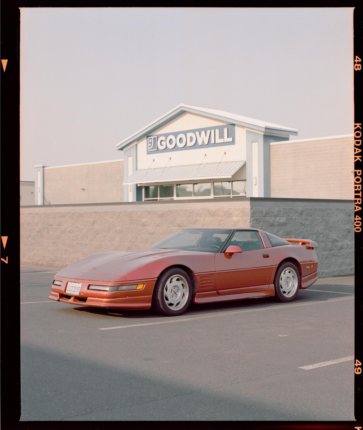 A red Corvette is parked in front of a Goodwill store.