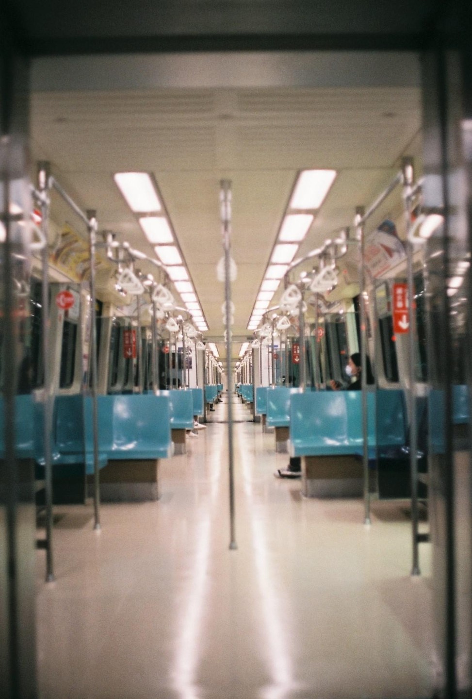 The interior of a subway car is shown with rows of empty blue seats and a few passengers visible in the distance.