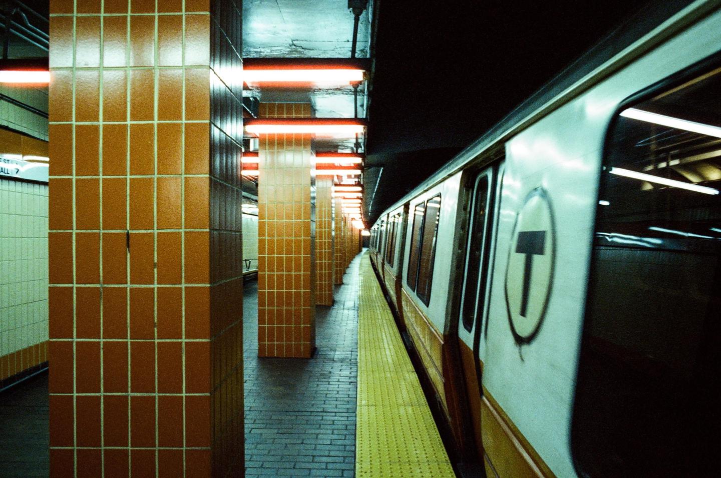 A subway train is stopped at a station platform with orange tiled pillars and neon lights.