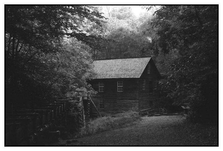 A wooden mill building with a water wheel is nestled among trees.