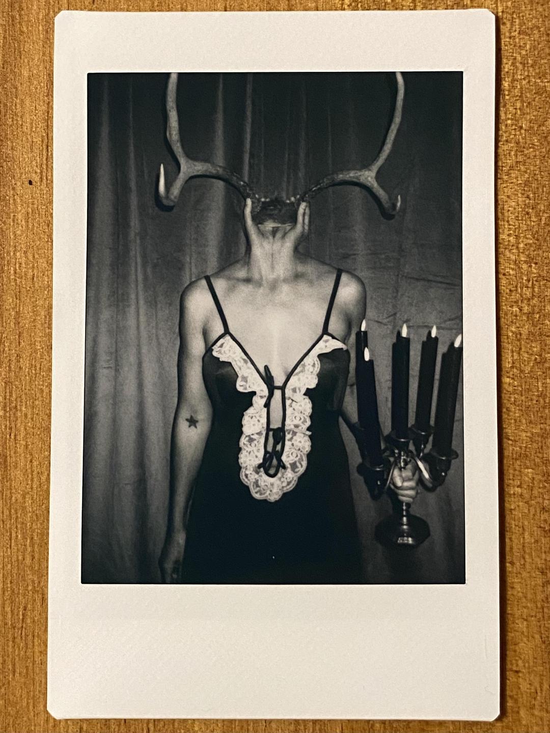 A woman with antlers for a head holds a candelabra with five lit candles.