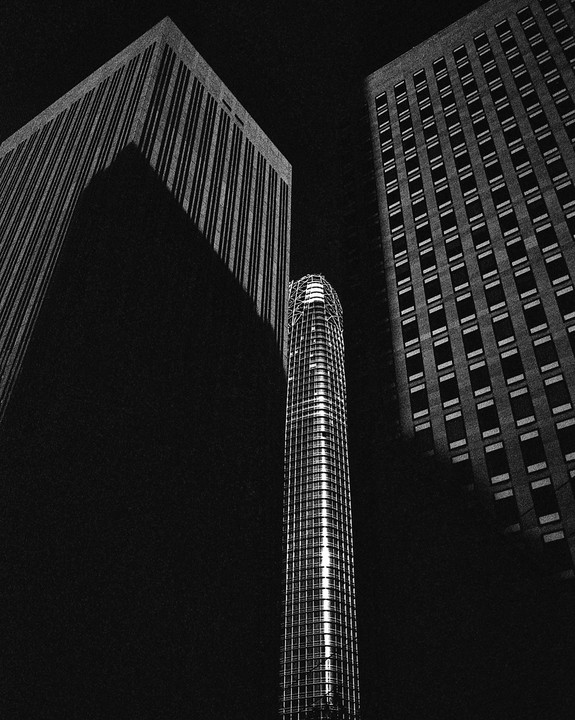 Three tall buildings are seen from below, with one in the center illuminated and the others in shadow.
