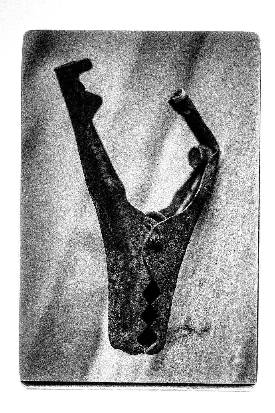 A rusty metal clamp is positioned upright against a textured surface.