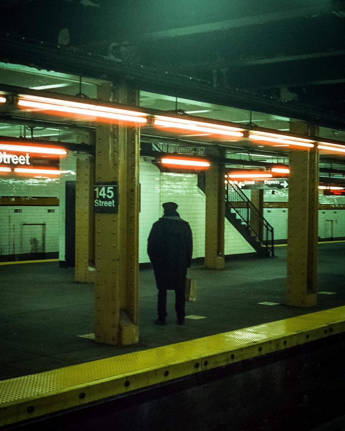 A man stands on a subway platform under orange lights.