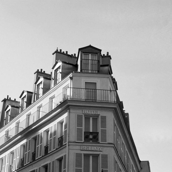 A black and white photograph shows the upper floors and roofline of a building with many windows and chimneys.