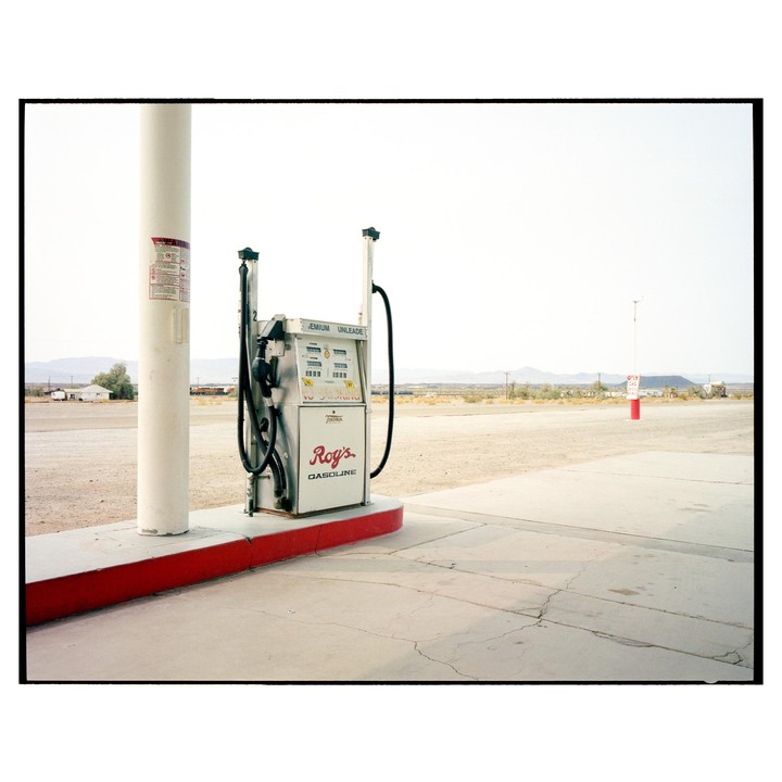 A vintage Roy's Gasoline pump stands at a desert gas station with mountains in the distance.