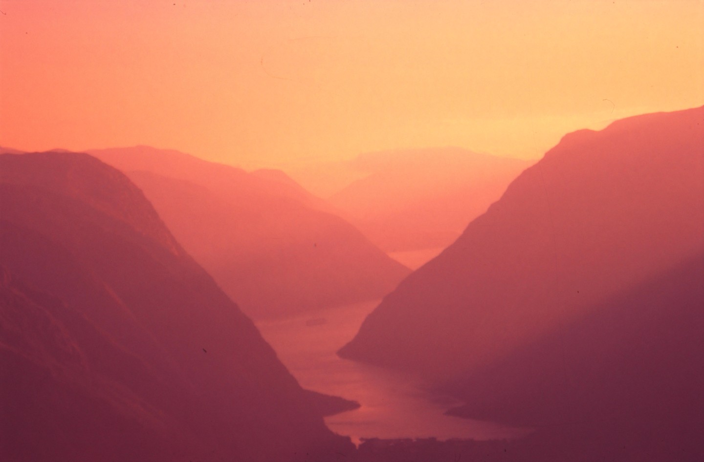 A river winds through a valley between mountains under a vibrant orange and pink sky.