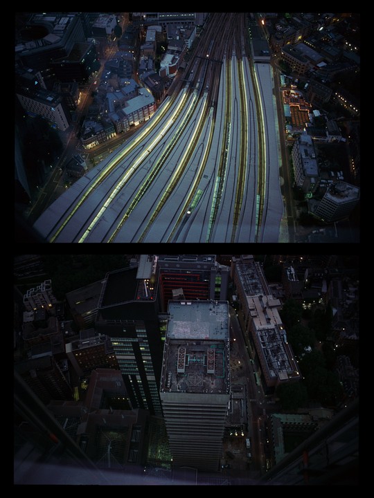 An aerial view shows a train station with multiple tracks and surrounding city buildings at night.