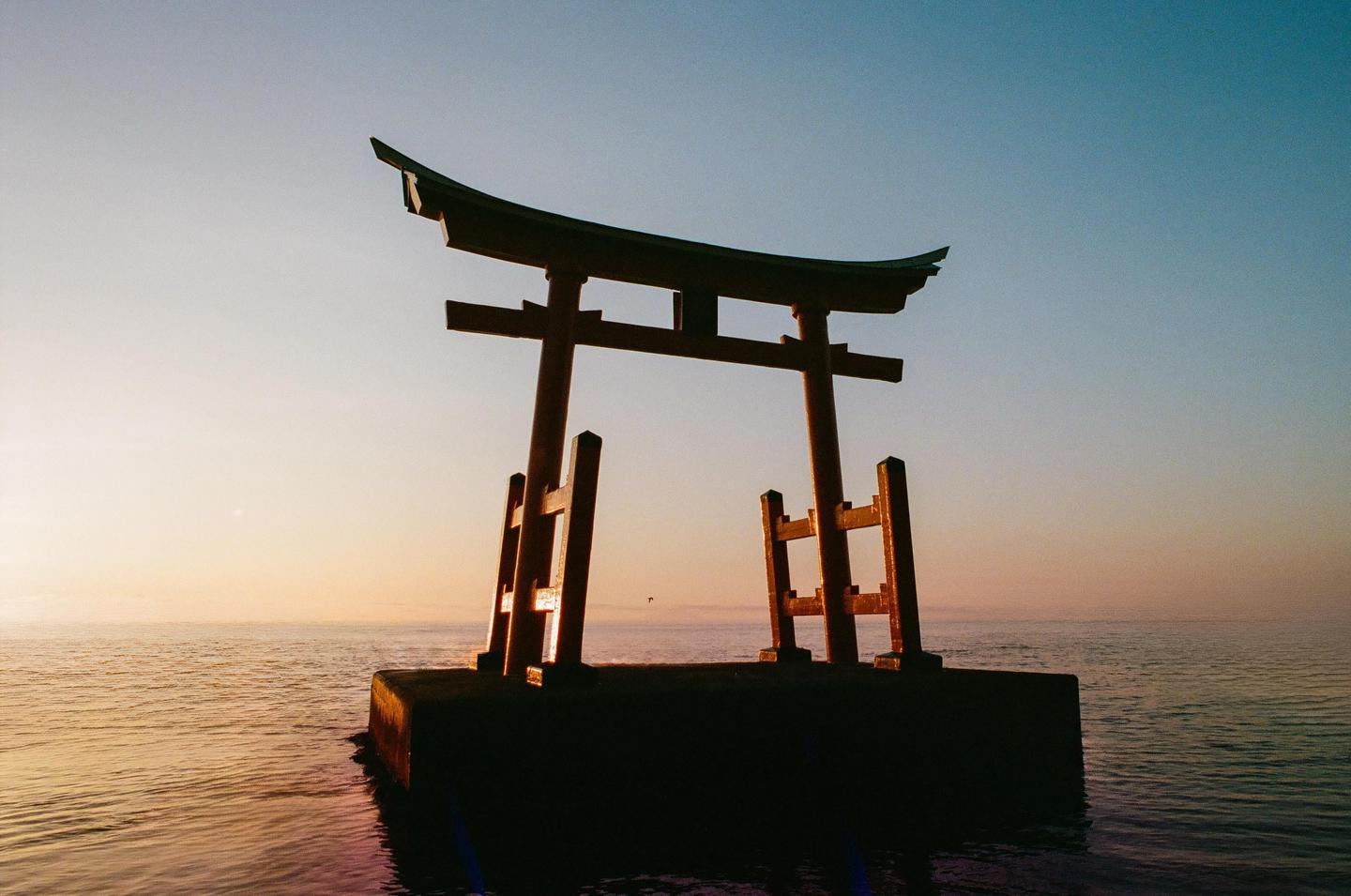 A torii gate stands in the water at sunset.