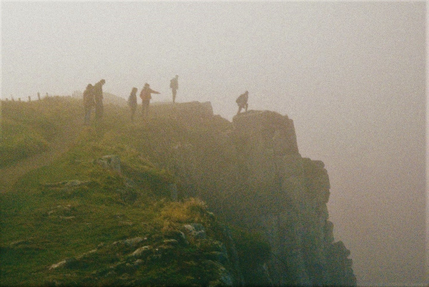 A group of people stand on a cliff edge in a hazy, green landscape.
