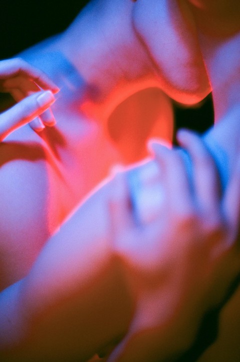 A person's hands and body are illuminated by red and blue light.