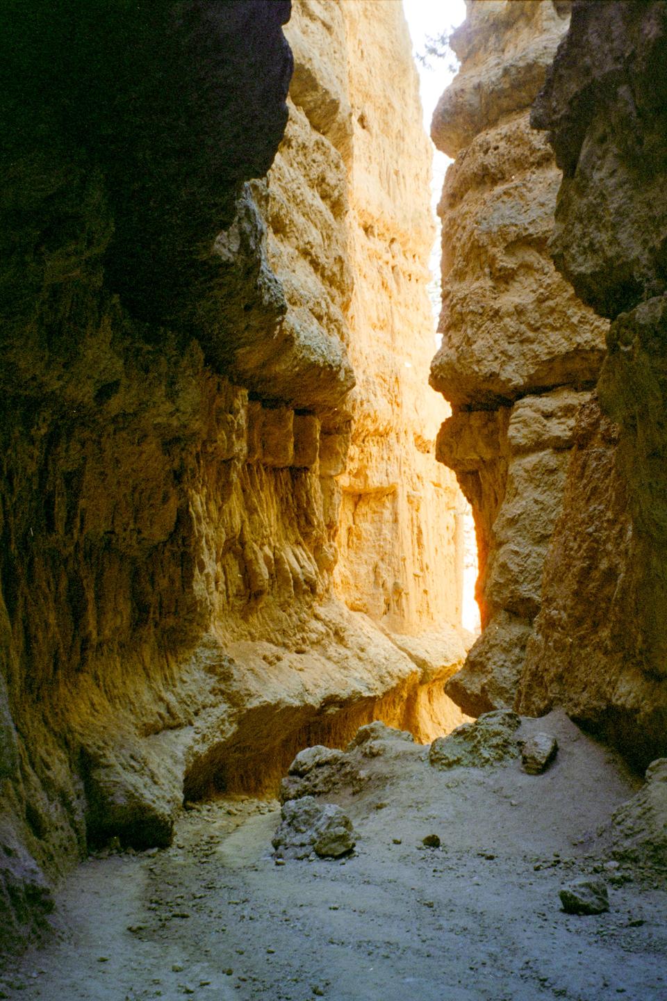 A narrow slot canyon with light shining through the opening.