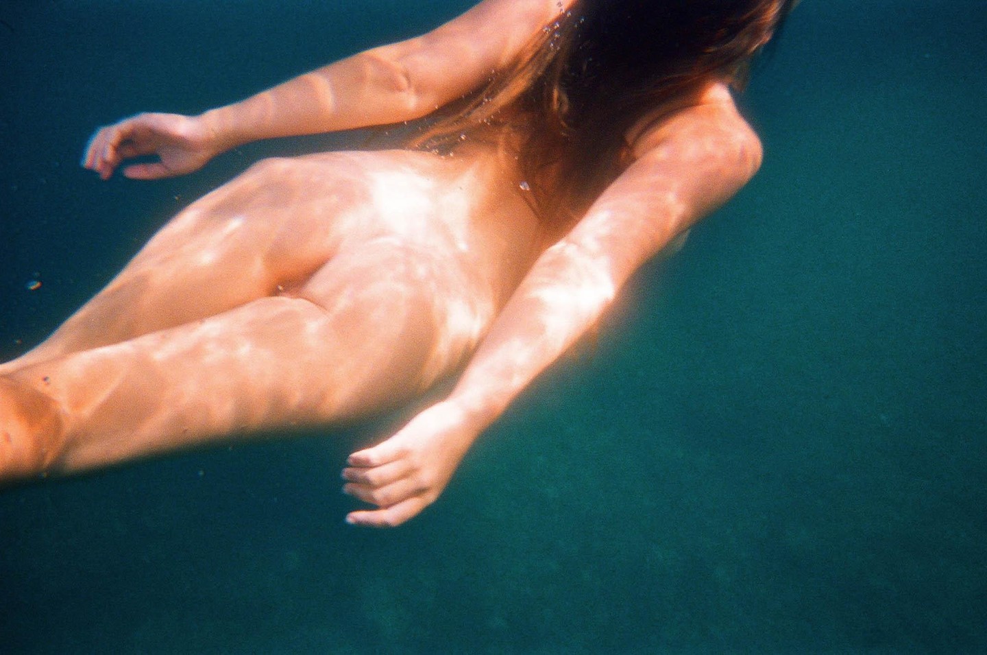 A woman swims underwater, with light patterns visible on her skin.
