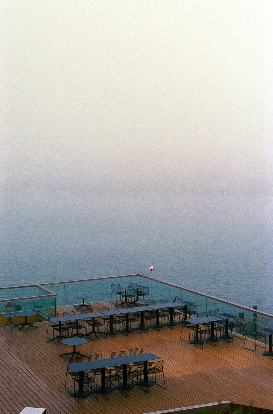 A restaurant patio with many tables and chairs overlooks a body of water under a hazy sky.
