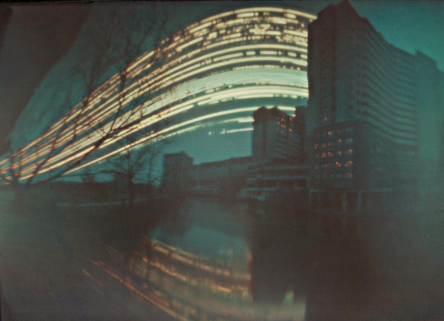 Light trails arc over a brutalist building and its reflection in water.