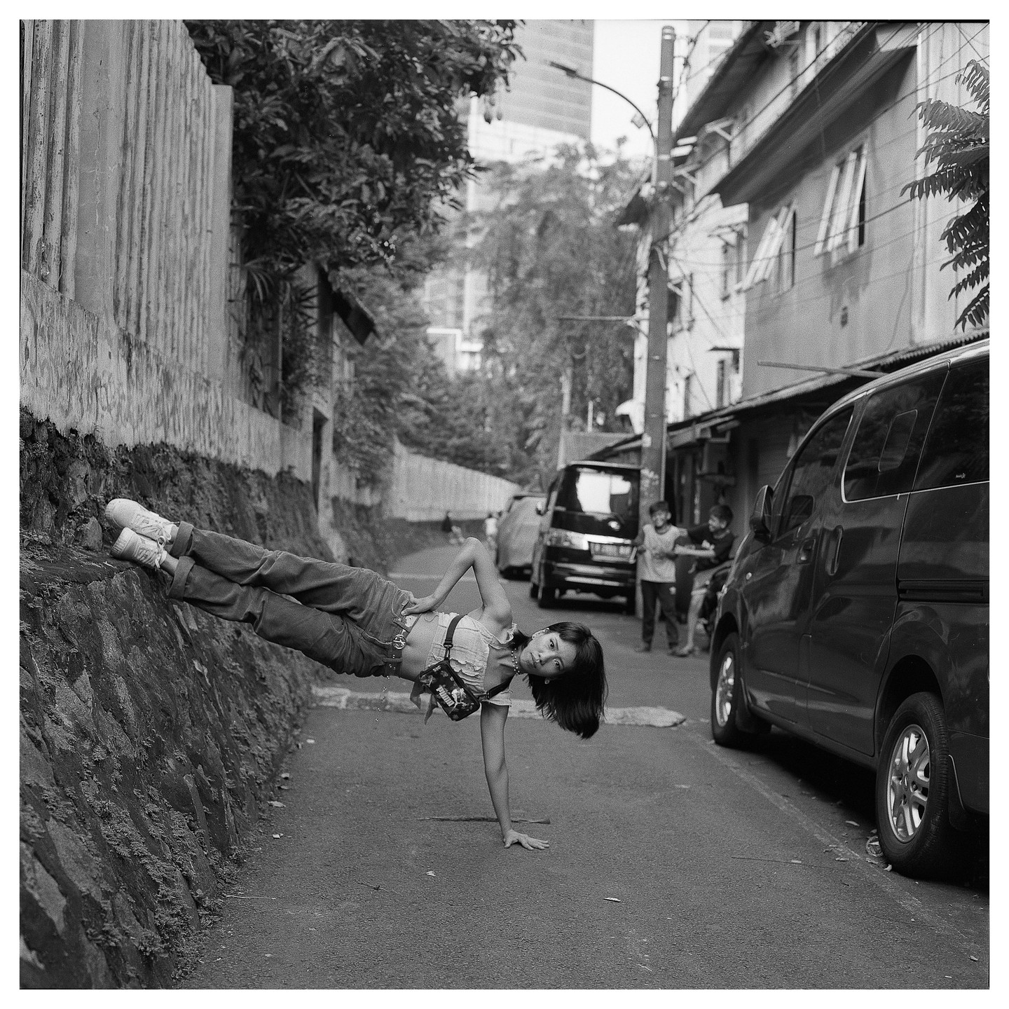 A woman balances on one hand and her feet against a stone wall on a street in Jakarta.