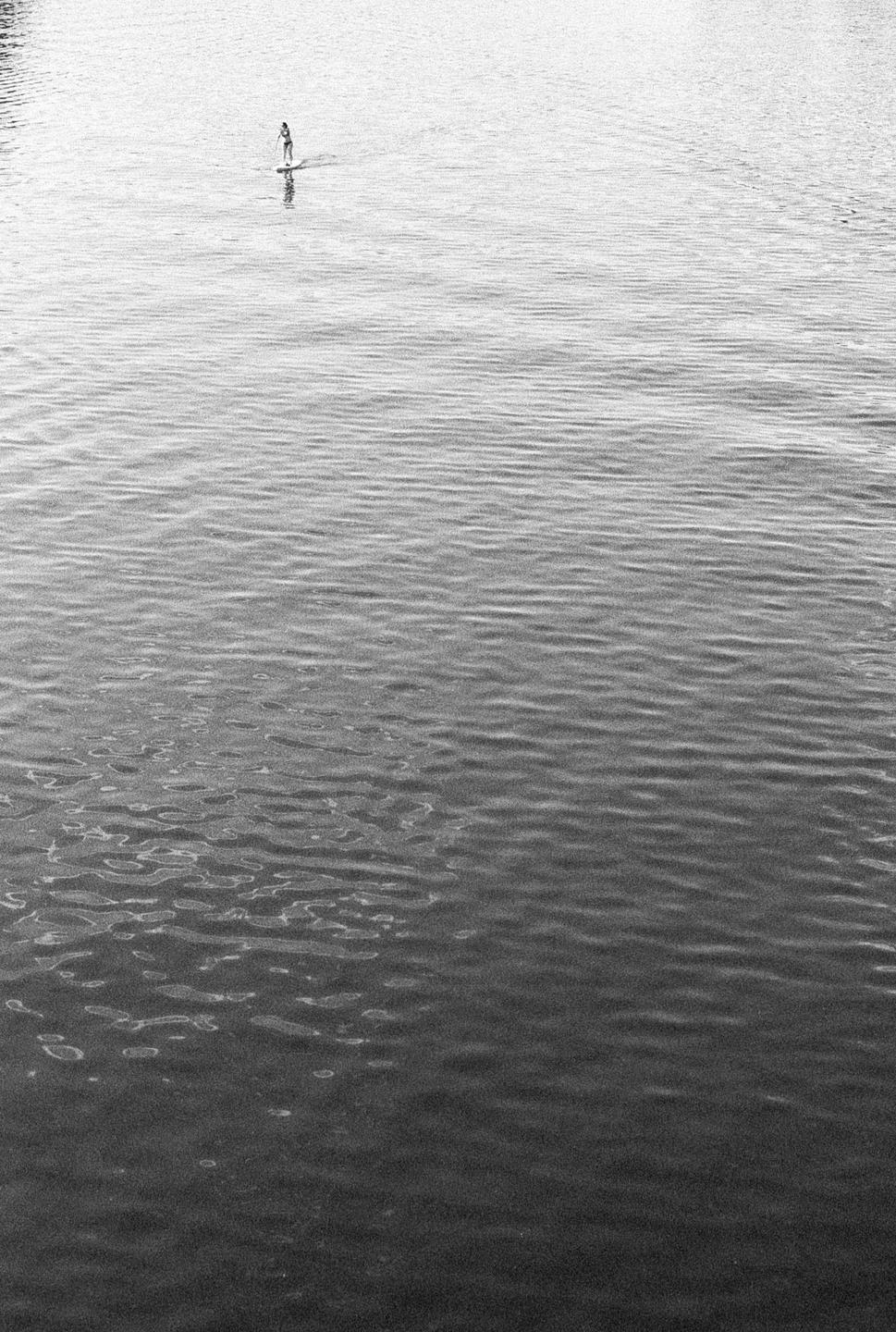 A person paddleboards on a body of water with ripples.