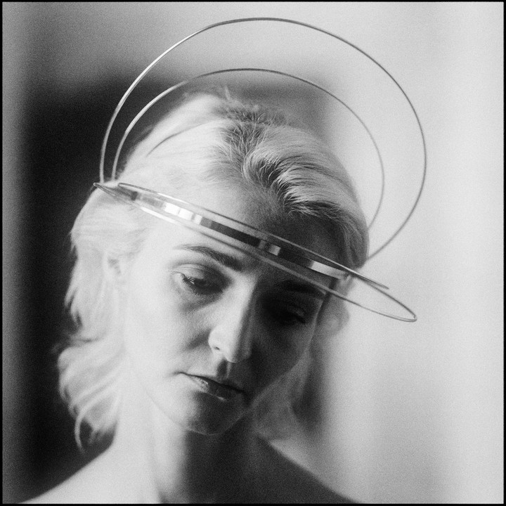 A woman with light hair looks down while wearing a circular metal headpiece.
