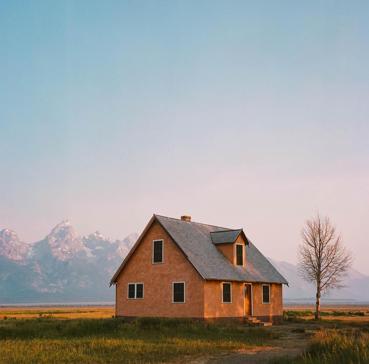 A house stands in a field with mountains in the background under a clear sky.