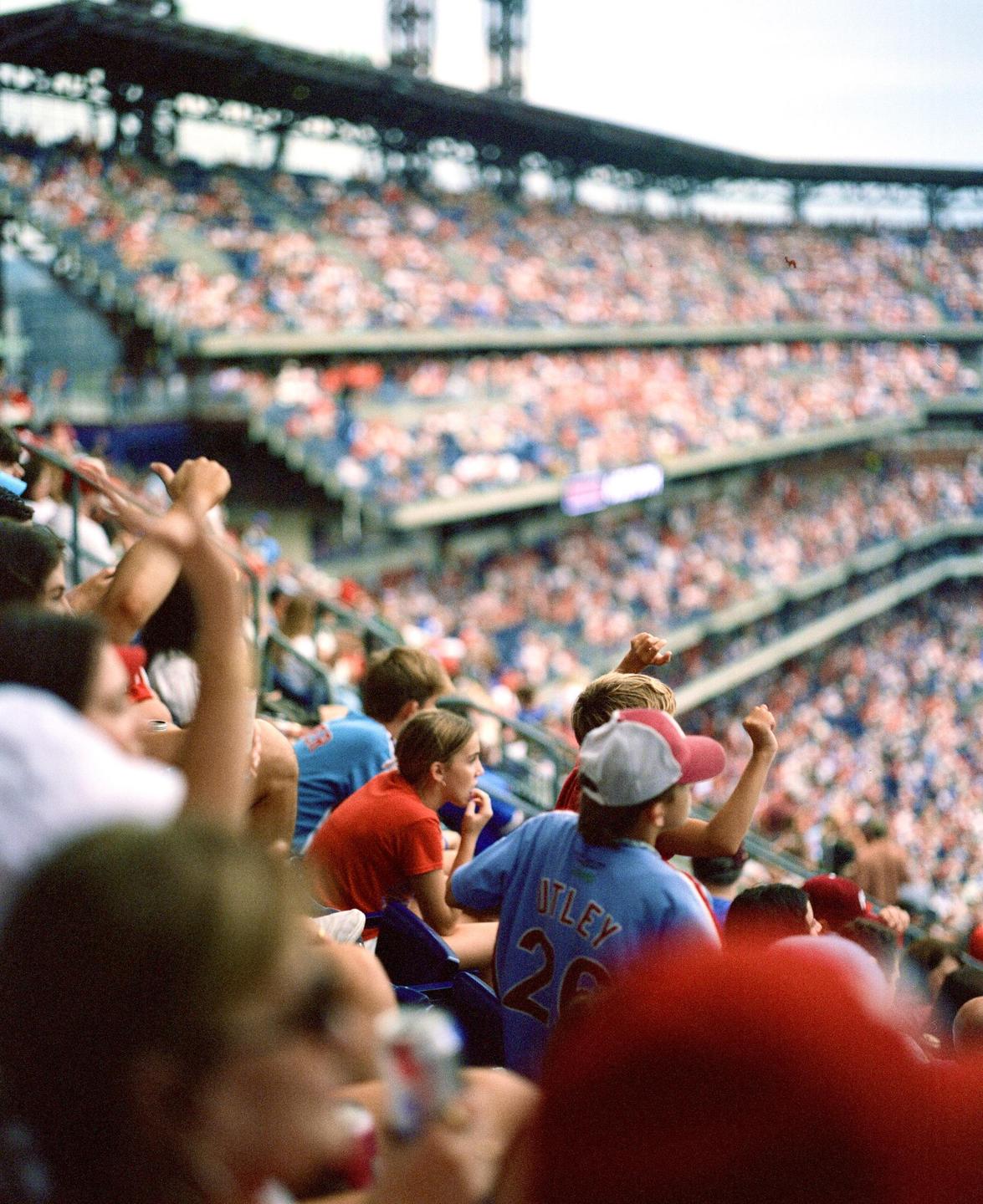 A crowd of baseball fans watches a game from the stands of a stadium.