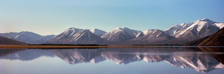 Snow-capped mountains are reflected in a calm lake under a clear sky.