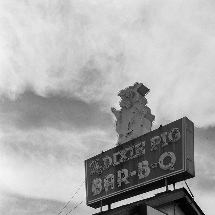 A large sign for "The Dixie Pig Bar-B-Q" with a pig character on top is visible against a cloudy sky.