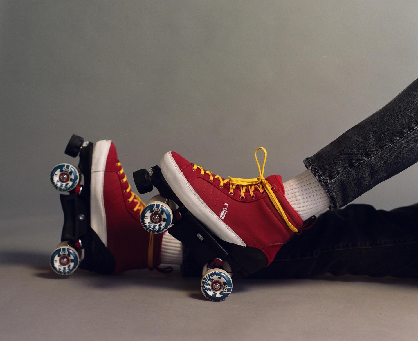 A person wearing red roller skates with yellow laces and black jeans is sitting on a gray surface.