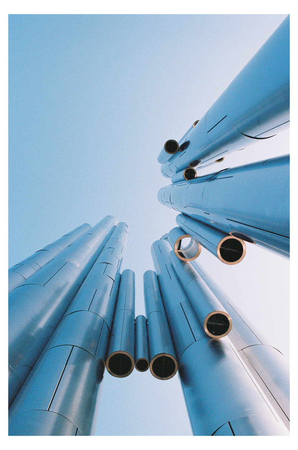 A low-angle view shows a cluster of metallic pipes against a clear blue sky.