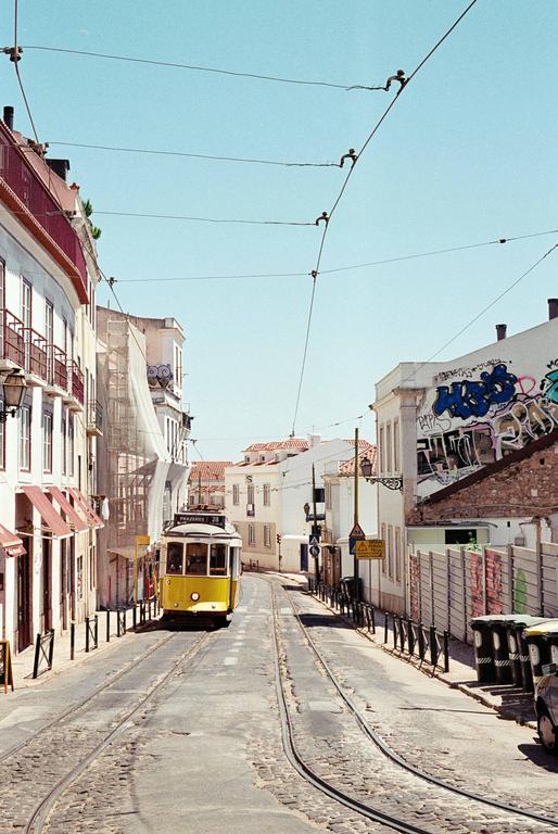 A yellow tram travels down a cobblestone street lined with buildings and overhead wires.